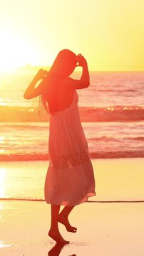 Attractive Asian woman enjoys a walk on the beach at sunset in Southern California. Slow Motion. Vertical Video.