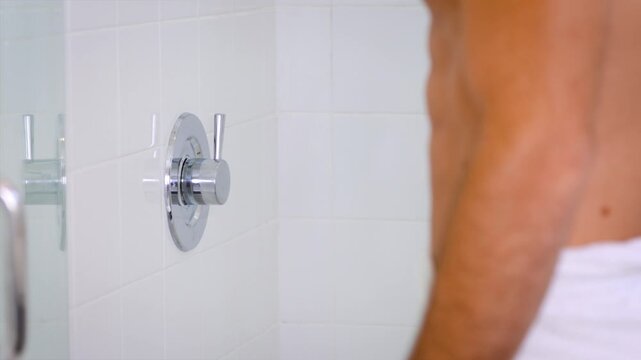 Close-up of a man's hand turning on the shower before entering.
