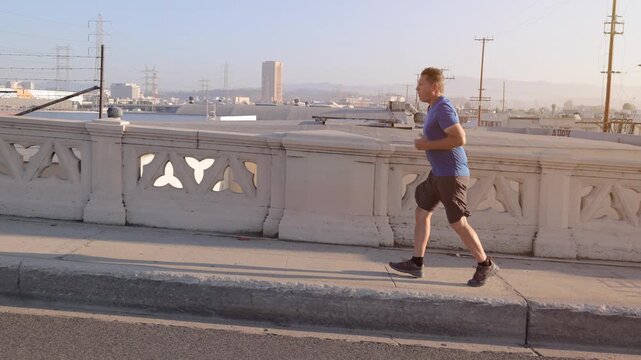 Middle-aged man, working on getting back into shape, jogging across one of the many bridges over the LA River near downtown Los Angeles.