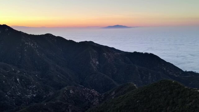 Aerial shot of mountains rising above a layer of low clouds at sunrise. Southern California.
