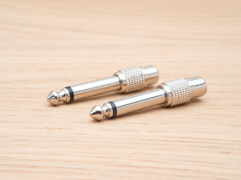 Two Silver Audio Jack Connectors - Two silver audio jack connectors, also known as phone plugs or TS connectors, are arranged diagonally on a light wood grain background.