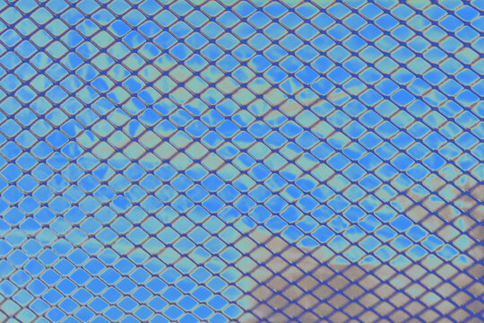 Abstract background of metallic diamond mesh grid pattern over iridescence holographic blue foil surface.