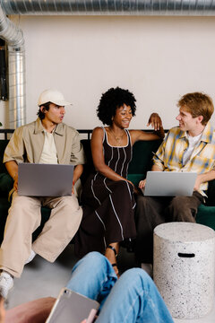 Three young office workers interacting and using laptops in a lounge.