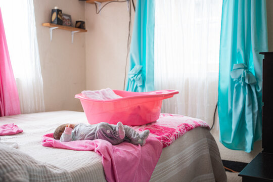 Baby sleeping on bed next to infant bathtub