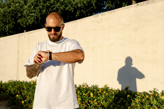 Bold man checking smartwatch outdoors with shadow and sunglasses