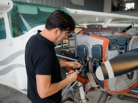 Mechanic Works on Small Airplane Engine in Hangar