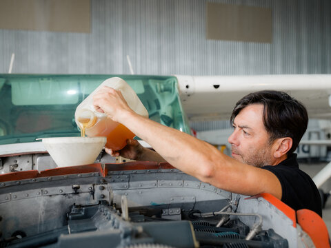 Mechanic is changing engine oil in airplane at hangar