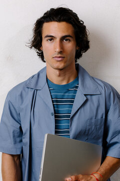 Young businessman with a laptop looking determined at the camera.