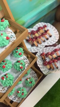 Holiday treats displayed on wooden trays. Green frosted cupcakes with red berries. Mini appetizers with cherry glaze. White lace doilies under each dish
