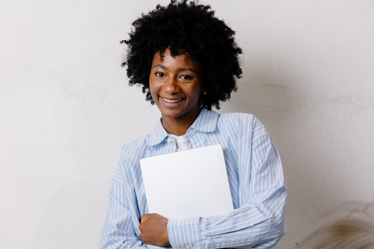 Medium shot portrait of a black woman with afro, holding a computer