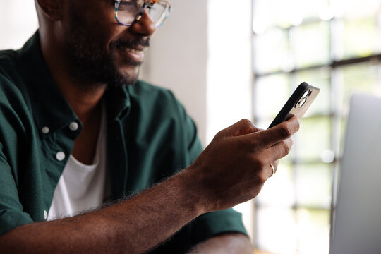 Smiling Man Using Smartphone While Working On Laptop
