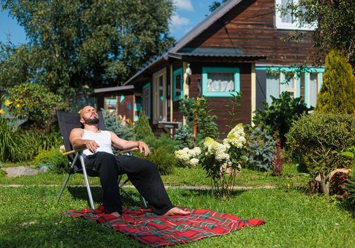 Man Relaxing in a Garden Near a Wooden House on a Sunny Day