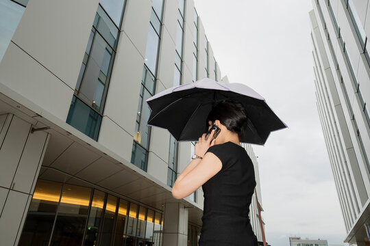 Businesswoman Making Phone Call Under Umbrella