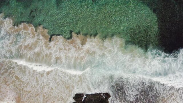 An ocean wave breaks along a turquoise coloured, pristine, reef-lined sandy shore. Filmed on a beautiful idyllic sunny day from high above the beach on the South Coast of New South Wales, Australia.