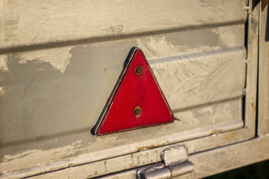 A red triangular reflector is fixed on the surface of a gray metal box. This view shows details of the box and reflects light in a rural area. The setting has natural light and is outdoors