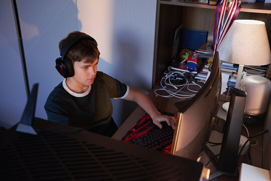 Teenage Boy Playing Computer Game with Headphones at Home