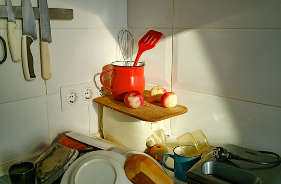 Still life on a messy kitchen counter with apples and a red mug