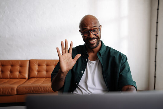 Smiling Man Waving During Remote Video Call At Home