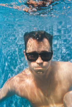 Man Swimming Underwater in a Pool While Wearing Sunglasses