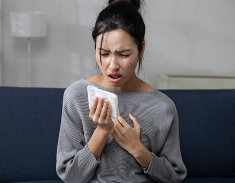 The young woman sat on the sofa in the living room, clutching her chest in obvious discomfort, possibly indicating heartburn. She also had a cough, sore throat, and runny nose.
