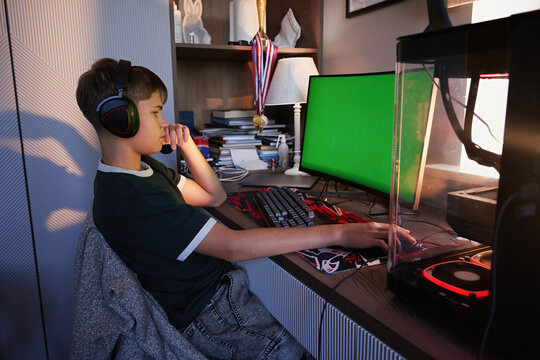 Teenage Boy Playing Computer Game with Headphones at Home