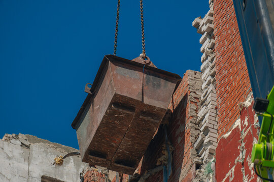 Close-up of a metal crane bucket clearing construction debris during the demolition of a damaged building.