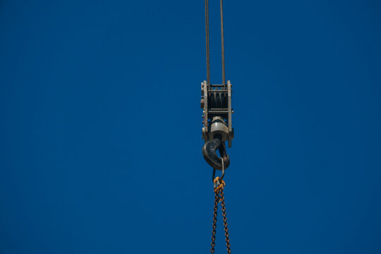 Close-up of a heavy construction crane hook block with steel cables and chains against a clear blue sky.