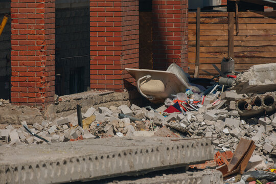 Close-up of a destroyed residential site with a bathtub lying among concrete slabs and brick rubble after a blast.
