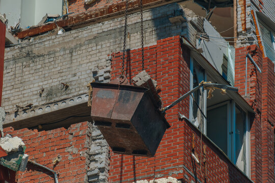 Close-up of a metal crane bucket filled with brick and concrete rubble during demolition work at a destroyed residential building site.