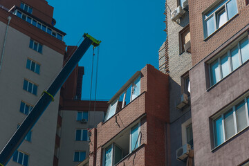 Crane boom extended against the facade of a damaged multi-story brick residential building after explosion under blue sky. © Denis Chubchenko