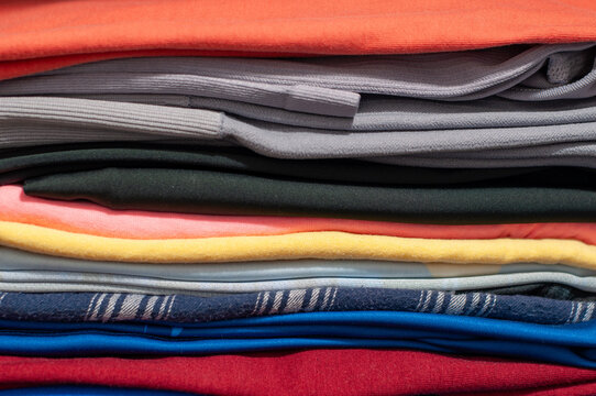 Full-frame close-up shot of a neat stack of folded colorful t-shirts and shirts. Wardrobe organization, laundry care, and textile background concept.