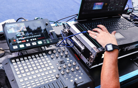 Video production operator controlling professional live streaming and audiovisual equipment with laptop and video switcher during an event