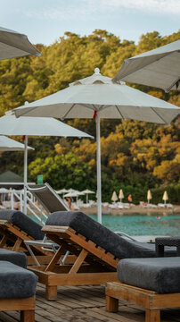 Sun loungers with white umbrellas on a wooden deck overlooking a serene turquoise sea bay