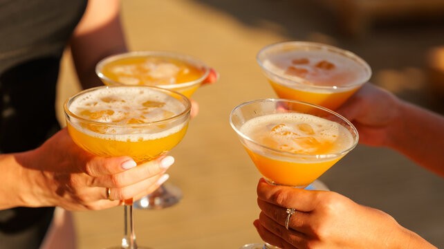 Friends holding orange cocktails in glasses during a sunny outdoor social gathering at sunset