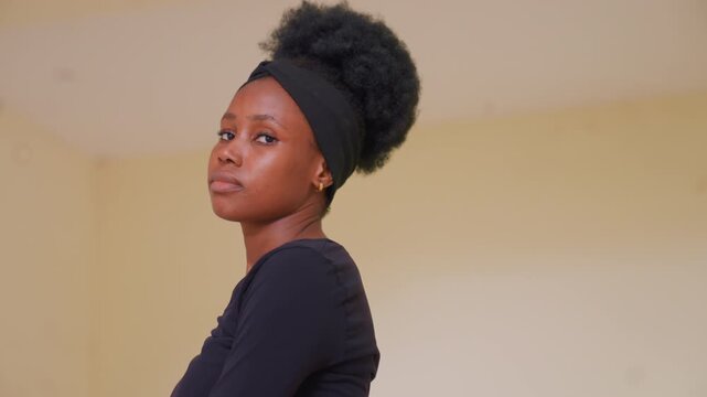 Young black woman wearing dark clothing and headband faces forward against plain beige walls. Her posture is steady without significant motion or interaction