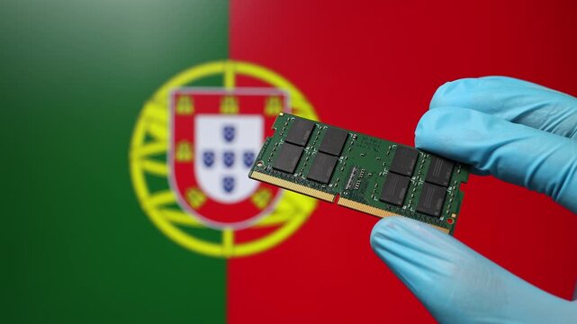 Close up view of hand in blue glove holding RAM memory microchip module. Portuguese flag in blurred background. Concept of semiconductor shortage, artificial intelligence development in Portugal.