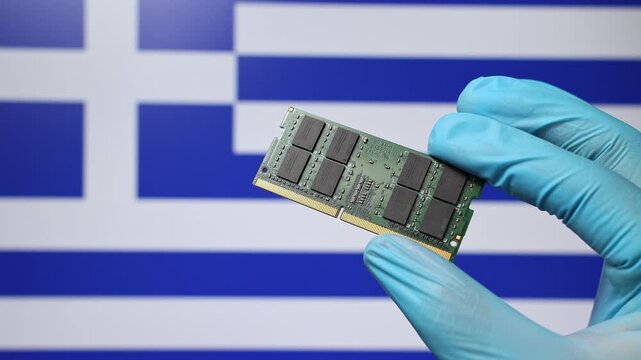 Close up view of hand in blue glove holding RAM memory microchip module. Greek flag in blurred background. Concept of semiconductor shortage, artificial intelligence development in Greece.