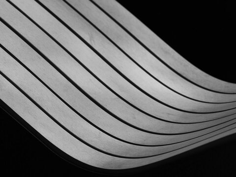 high contrast black and white photograph featuring a modern, curved surface with sharp, parallel lines that create a dynamic sense of motion against a dark background, park bench