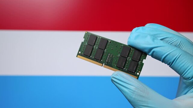 Close up view of hand in blue glove holding RAM memory microchip module. Luxembourgish flag in blurred background. Concept of semiconductor shortage, artificial intelligence development in Luxembourg.