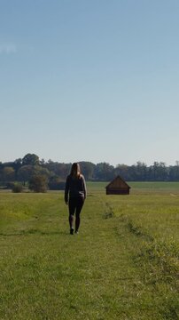 Woman walking through a scenic green meadow towards a traditional historic wooden hay barn in Trebon, Czech Republic
