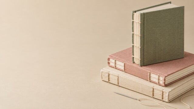 Linen Covered Coptic Journals Stacked with a Binding Needle on Cream