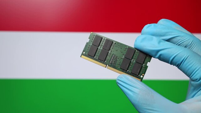 Close up view of hand in blue glove holding RAM memory microchip module. Hungarian flag in blurred background. Concept of semiconductor shortage, artificial intelligence development in Hungary.