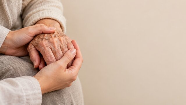 Younger hands gently cradling an older hand in a warm closeup portrait