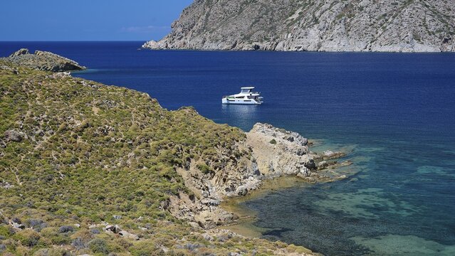 A boat lies on the turquoise sea next to a rocky shore in fine weather, Psili Ammos Srand, Patmos, Dodecanese, Greek Islands, Greece