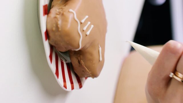 Vertical video. Garnishing pastry. Piping icing. Female confectioner hand drawing white lines sugar frosting decorating glazed gingerbread cookie.