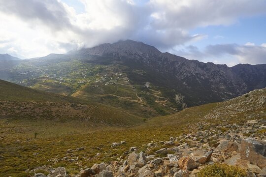 Spring in Crete, morning light, Thripti village on green mountain slope, grey mountain massif, cloudy sky, sun shining through clouds, overgrown slope and scree, Thripti mountain massif, Eastern Crete, Crete island, Greece