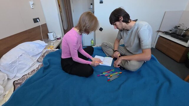 College students collaborate over written assignments on blue blanket, managing academic stress under pressure. Focused partners write in notebook, revising lecture notes thoughtfully together.