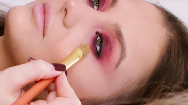 Vertical video. Beauty makeup. Visage salon. Female professional cosmetician applying product for radiant facial skin using brush at workplace.
