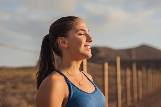 Woman enjoys outdoor wellness and fresh air with closed eyes at sunset. Her peaceful smile in a natural landscape supports mindfulness, relaxation, healthy living, mental health, and freedom campaigns