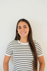 Young smiling woman poses for a remote work profile portrait against a plain indoor wall. Her warm expression suits freelancer, business, home office, technology, and online career communication. © Daniel
